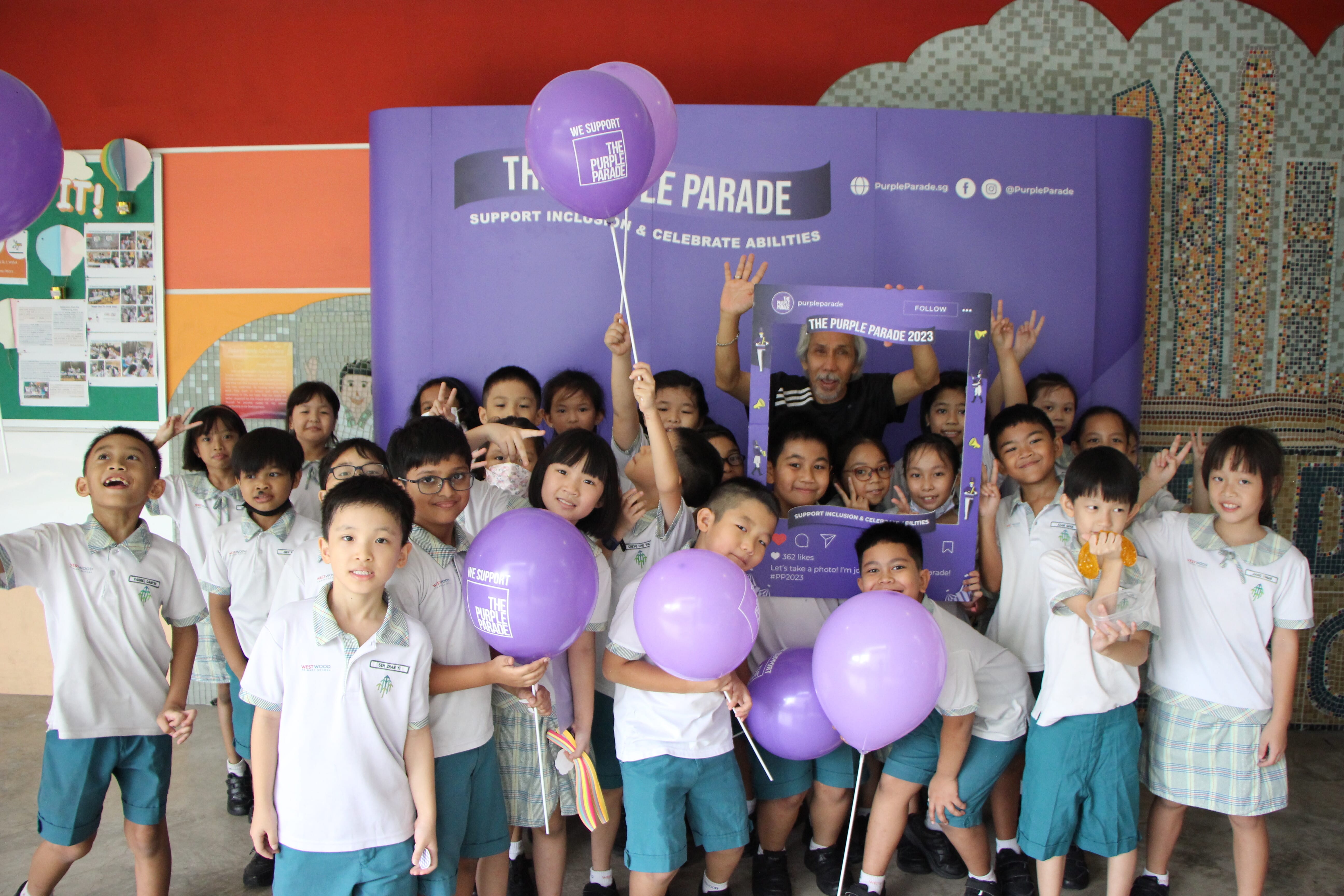 Group of uniformed schoolchildren and an adult posing with purple balloons in front of a Purple Parade 2023 banner.